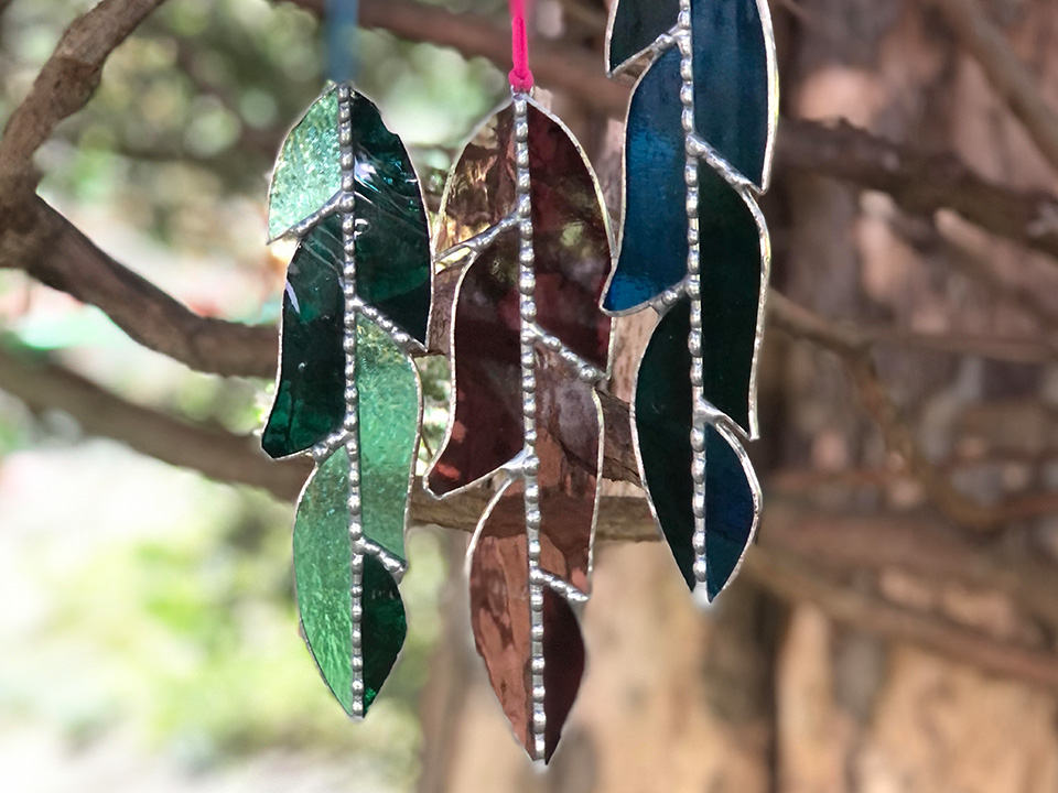 3 stained glass feathers hanging off tree branch