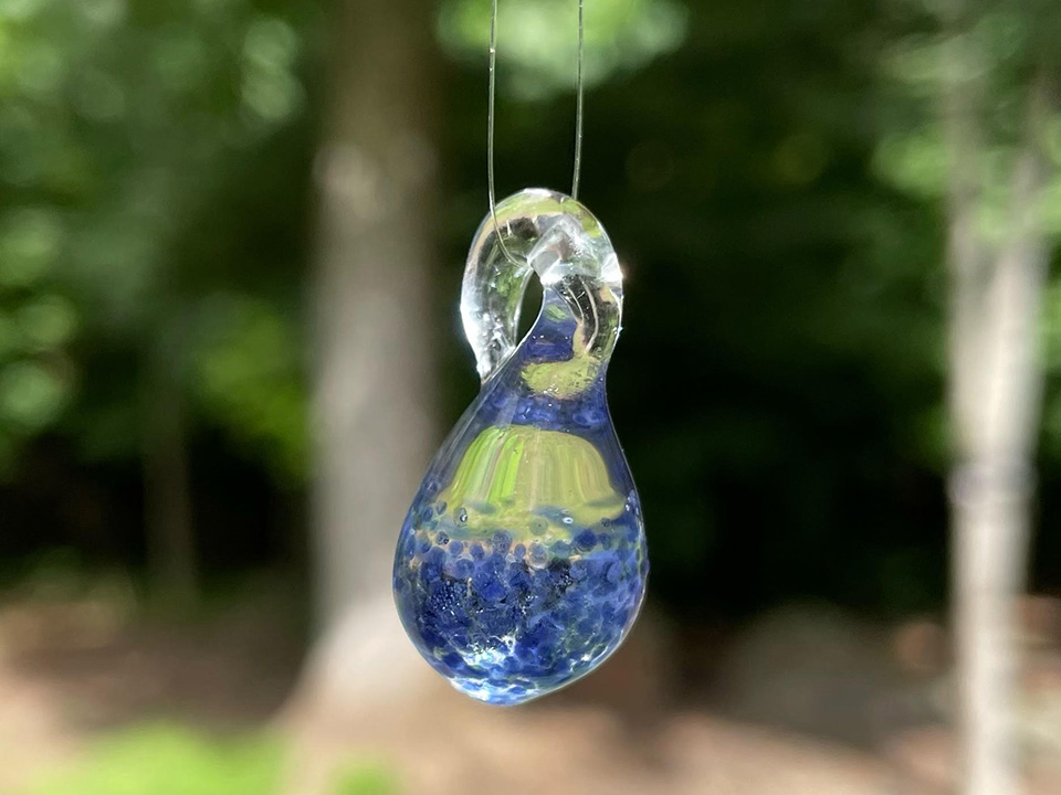 Blue colored glass pendant with trees in the background