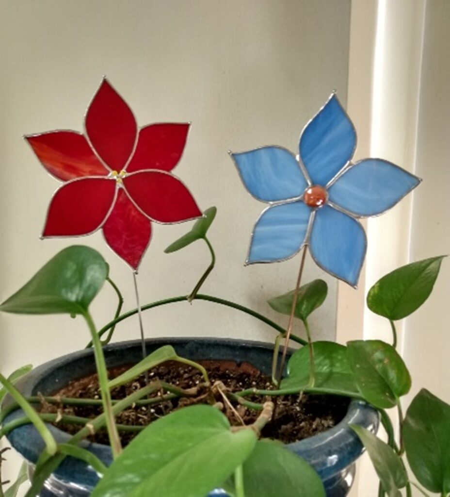 Stained glass red poinsettia and blue flower plant stakes in planter