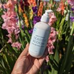 Hand holding lotion with a field of flowers in the background